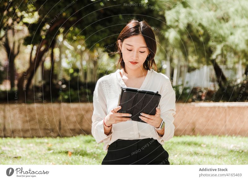 Junge ethnische Frau arbeitet aus der Ferne auf Tablet im Park Arbeit Tablette abgelegen achtsam neue Normale Coronavirus Job beschäftigt Apparatur benutzend