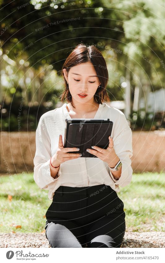 Junge ethnische Frau arbeitet aus der Ferne auf Tablet im Park Arbeit Tablette abgelegen achtsam neue Normale Coronavirus Job beschäftigt Apparatur benutzend