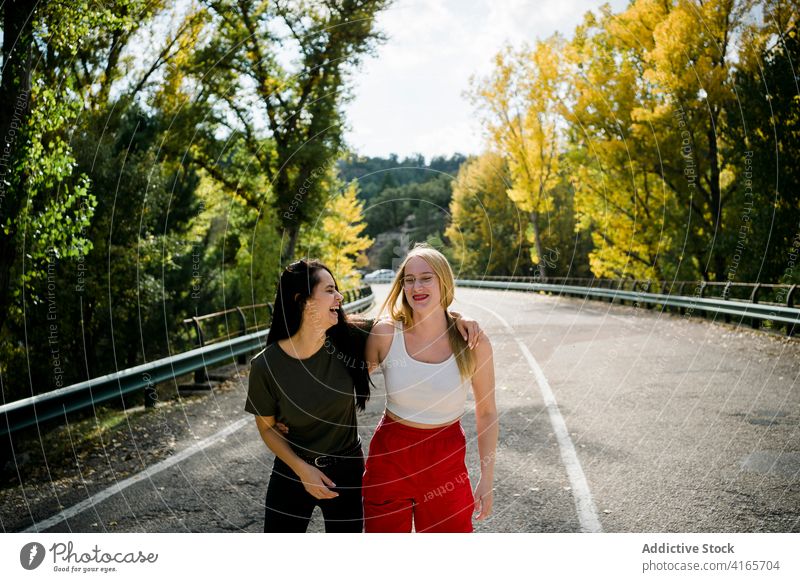 Glückliche Freundinnen umarmen sich auf der Landstraße Frauen Straße Wald Umarmung Herbst Freundschaft Landschaft Natur heiter jung Fahrbahn Zusammensein