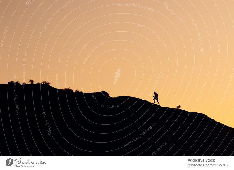 Anonyme Person, die bei Sonnenuntergang auf einem Hügel läuft laufen Berge u. Gebirge Berghang Training Athlet Aufstieg Silhouette Übung Gesundheit Sport