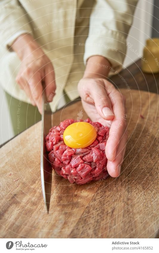 Crop-Köchin bei der Zubereitung von Steak Tartare roh Rindfleisch Koch Frau Küchenchef Ei Eigelb Fleisch Tradition rund Form Bestandteil Messer Lebensmittel