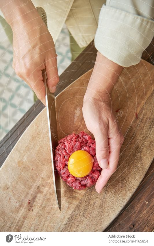 Crop-Köchin bei der Zubereitung von Steak Tartare roh Rindfleisch Koch Frau Küchenchef Ei Eigelb Fleisch Tradition rund Form Bestandteil Messer Lebensmittel