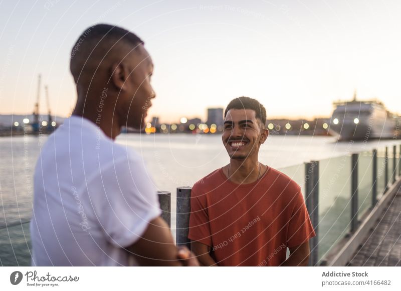 Junge fröhliche ethnische Freunde, die sich gegenseitig anlächeln Männer Zusammensein Freundschaft positiv froh Spaß Fluss Stauanlage sich[Akk] entspannen