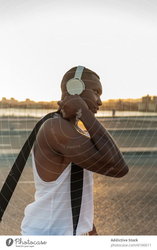 Schwarzer Sportler mit Kopfhörern beim Ausruhen nach dem Training Mann Athlet ernst muskulös sportlich Musik zuhören passen männlich Sportbekleidung Lifestyle