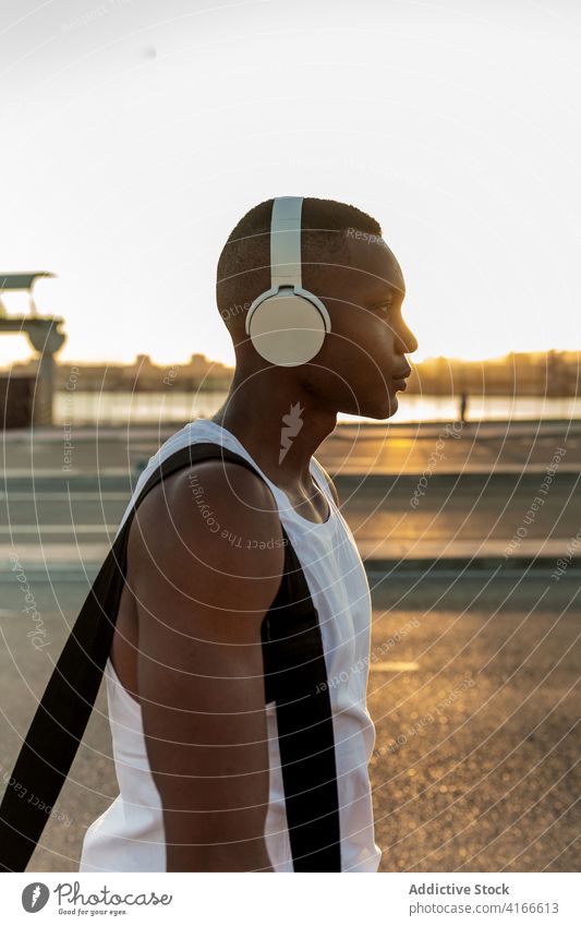 Schwarzer Sportler mit Kopfhörern beim Ausruhen nach dem Training Mann Athlet ernst muskulös sportlich Musik zuhören passen männlich Sportbekleidung Lifestyle