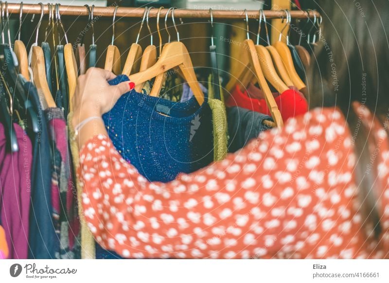 Junge Frau stöbert durch Klamotten auf einer Kleiderstange im Second Hand Laden oder auf dem Flohmarkt. Kleidung stöbern Anziehsachen bunt shopping