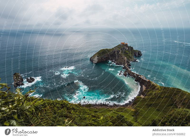 Gekräuseltes Meer in der Nähe von grünen Berg mit Gehweg unter Himmel Berge u. Gebirge Gaztelugatxe Natur Hochland San Juan Meereslandschaft Atmosphäre Laufsteg