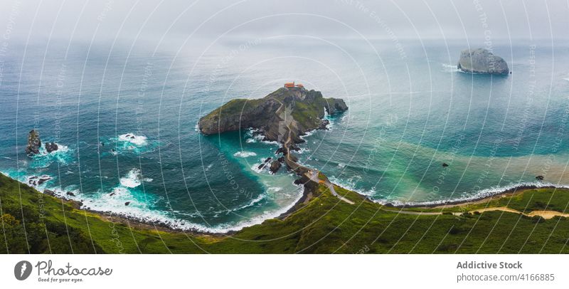 Gekräuseltes Meer in der Nähe von grünen Berg mit Gehweg unter Himmel Berge u. Gebirge Gaztelugatxe Natur Hochland San Juan Meereslandschaft Atmosphäre Laufsteg