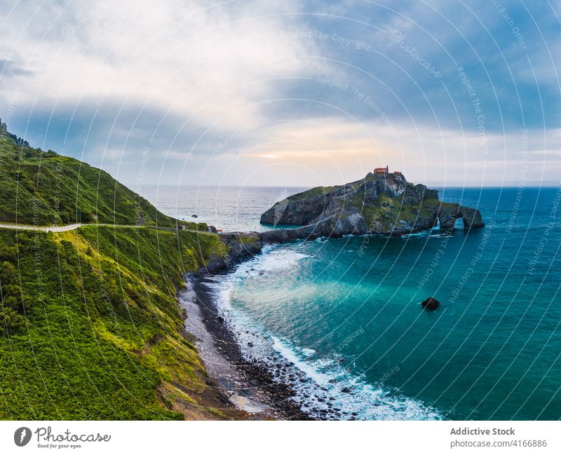 Gekräuseltes Meer in der Nähe von grünen Berg mit Gehweg unter Himmel Berge u. Gebirge Gaztelugatxe Natur Hochland San Juan Meereslandschaft Atmosphäre Laufsteg