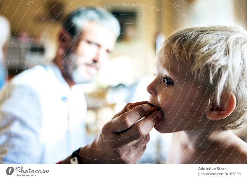 Vater füttert süßes Kind zu Hause Mann Futter essen Snack Partnerschaft Pflege Liebe abstützen Eltern Zuneigung bezaubernd hungrig Sohn blond heimwärts sonnig