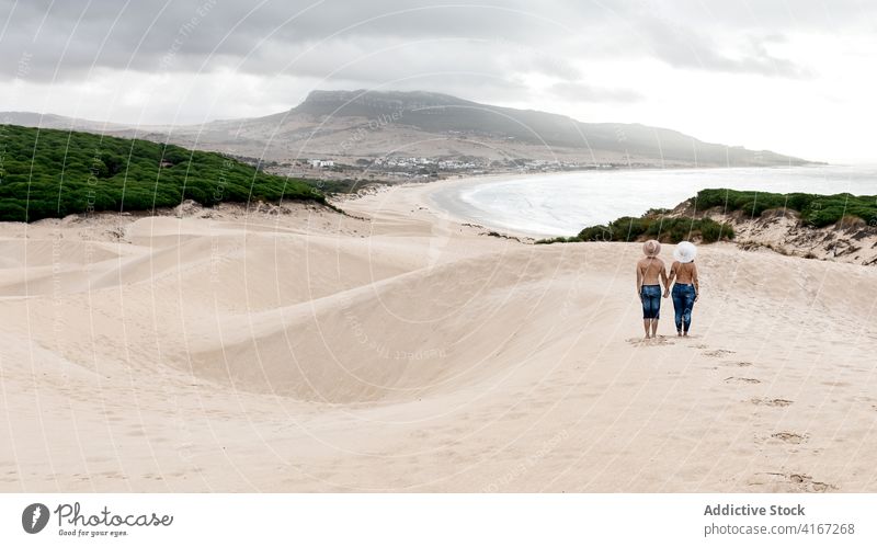 Unerkennbares Paar ohne Hemd, das sich an den Händen hält und an einer sandigen Küste steht oben ohne Meeresufer Strand erstaunlich ruhig Hafengebiet