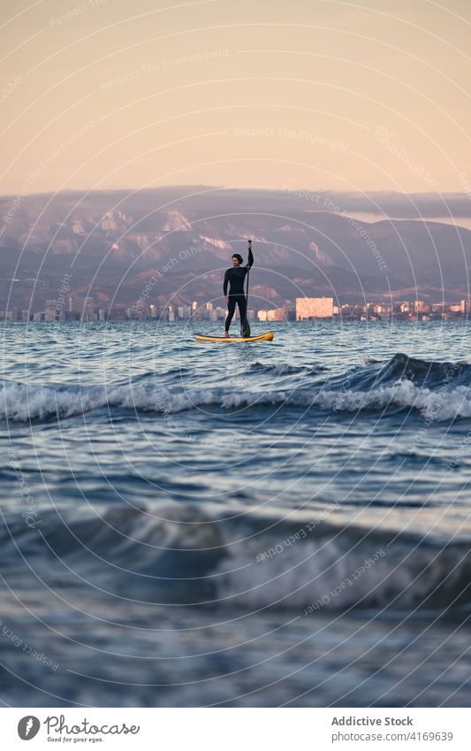 Mann im Neoprenanzug auf Paddleboard im Meer Paddelbrett Surfer Reihe Brandung SUP MEER Training männlich Sommer Sport Wasser Sonnenuntergang Natur genießen