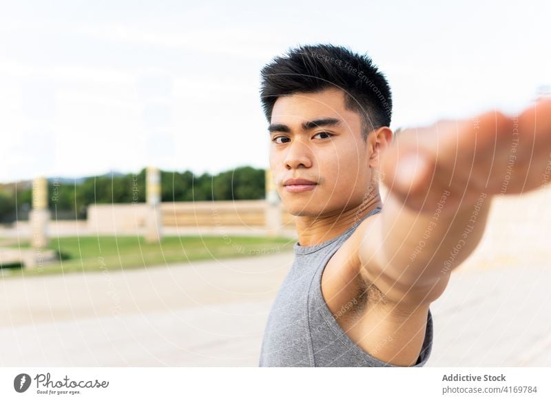 Ethnischer Mann in Sportkleidung macht Yoga bei Sonnenuntergang Krieger-Pose üben Asana beweglich Fokus ruhig männlich ethnisch asiatisch virabhadrasana urban