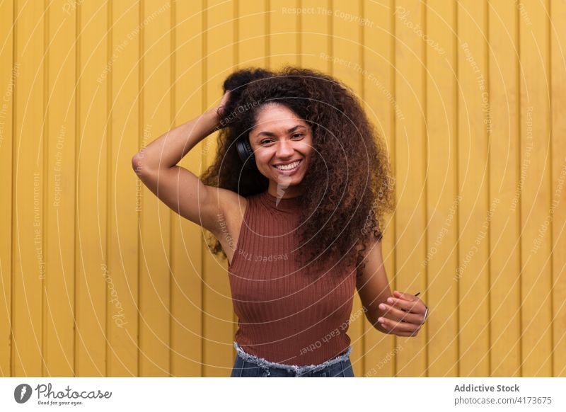 Charmante ethnische Frau mit Kopfhörer auf der Straße krause Haare Afro-Look Frisur charmant Lächeln natürlich Schönheit zuhören schwarz Afroamerikaner