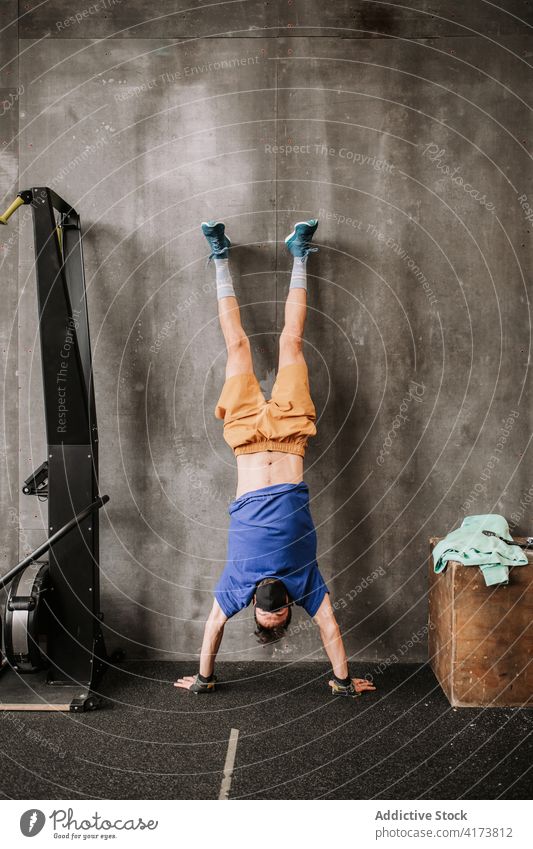 Sportler mit Maske im Handstand in der Turnhalle Wand Fitnessstudio Training Gleichgewicht Mundschutz neue Normale stark männlich modern Gesundheit anstrengen