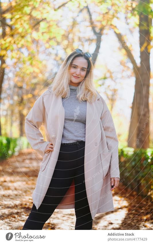 Junge Frau im Mantel im Herbst Park Outfit Lächeln schlendern Wochenende lässig jung heiter Glück Optimist Hand auf der Taille Freude trendy angenehm froh