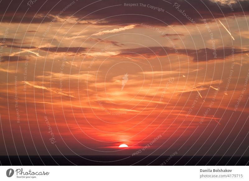 schöner Blick auf die Sonne, die sich hinter der Meeresoberfläche versteckt. Der Himmel ist bei Sonnenuntergang orange mit Wolken und Kondensationsspuren