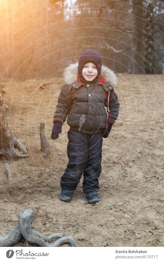 glücklich lächelnden Jungen in warmer Kleidung und Hut bedeckt seinen Hals vor kaltem Wind llooking at Kamera im Herbst im Freien Zähne Smiley Mantel blau