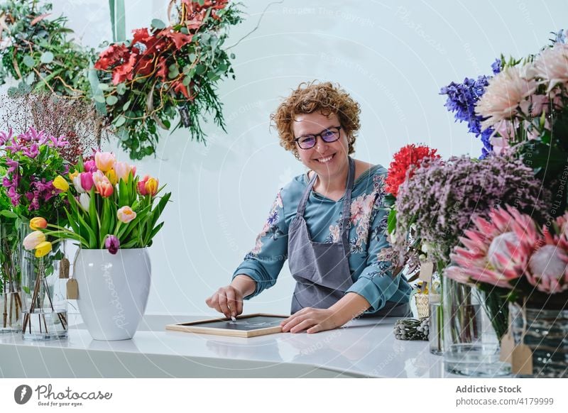 Frau schreibt auf Kreidetafel in Blumenladen schreiben Tafel Blumenhändler Weihnachten Feiertag Werkstatt vorbereiten Aufschrift kreativ Laden Winter Job Beruf