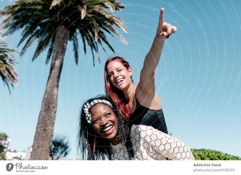 Fröhliche Freundinnen haben Spaß an einem Sommertag Huckepack Zeigen Sie weg heiter Spaß haben Zusammensein lesbisch Glück Mitfahrgelegenheit Frauen