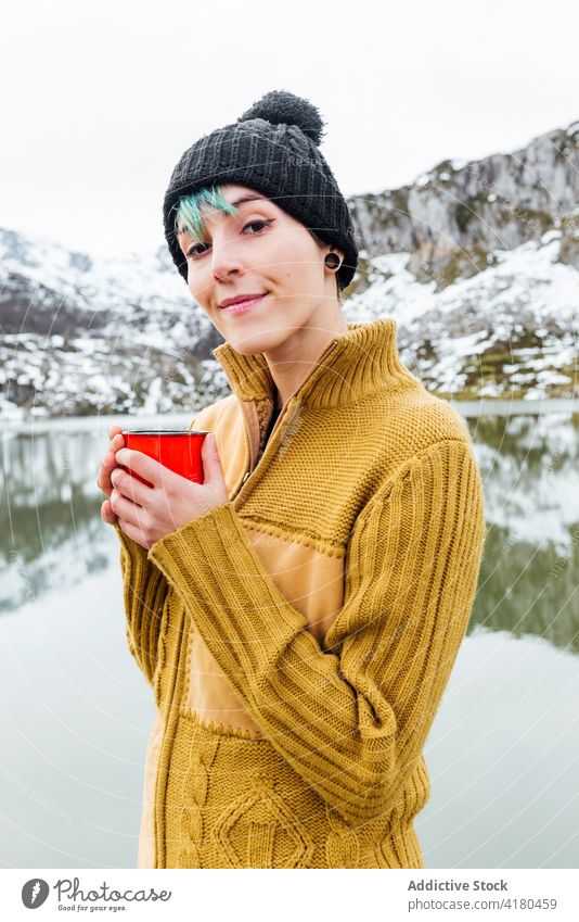 Gelassene Frau genießt heißes Getränk in der Nähe eines Sees in bergigem Terrain Berge u. Gebirge trinken Heißgetränk Gelassenheit genießen friedlich Winter