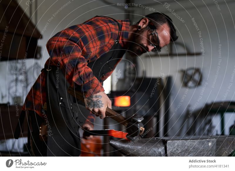 Fokussierter junger Schmied beim Erhitzen und Schlagen von Metall auf dem Amboss in der Werkstatt Mann Hufschmied Treffer bügeln Schmiede Funken manuell Hammer