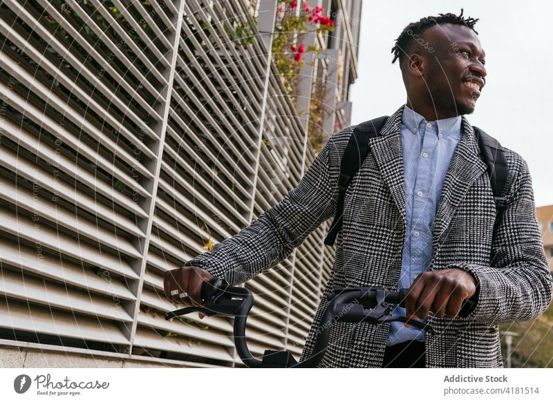 Fröhlicher schwarzer Büroangestellter mit Fahrrad auf einer Stadtstraße Mann heiter formal Stil Fahrzeug Straßenbelag freundlich Afroamerikaner Wand gerippt