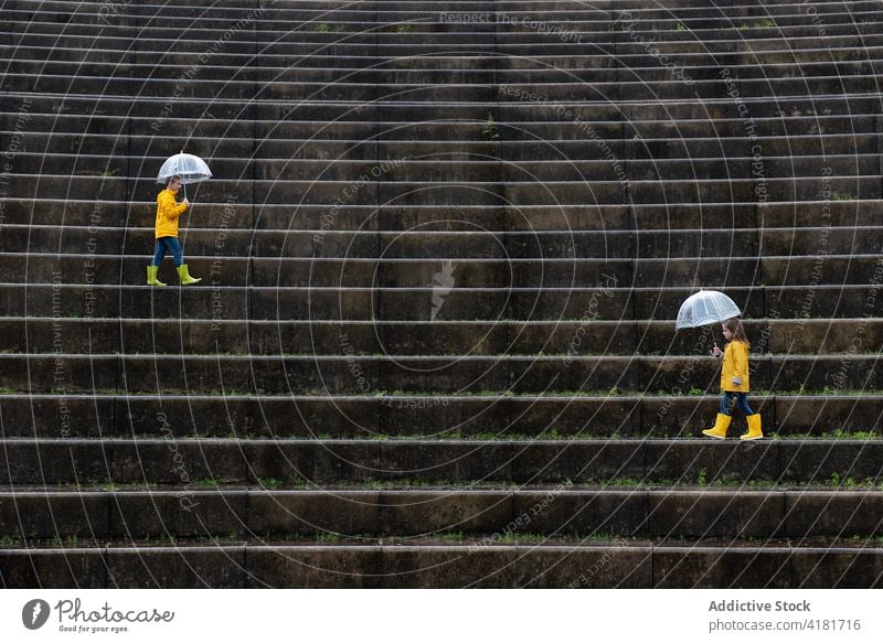 Kinder unter Regenschirmen, die an einem regnerischen Tag eine Treppe in der Stadt entlanglaufen gelb Regenmantel Spaziergang nass Zusammensein Herbst