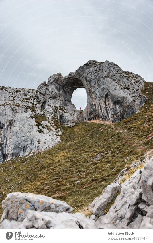 Entfernter Reisender in natürlichem Felsbogen stehend Felsen Golfloch Bogen erkunden Berge u. Gebirge Formation wolkig Fernweh Natur Asturien Spanien Abenteuer