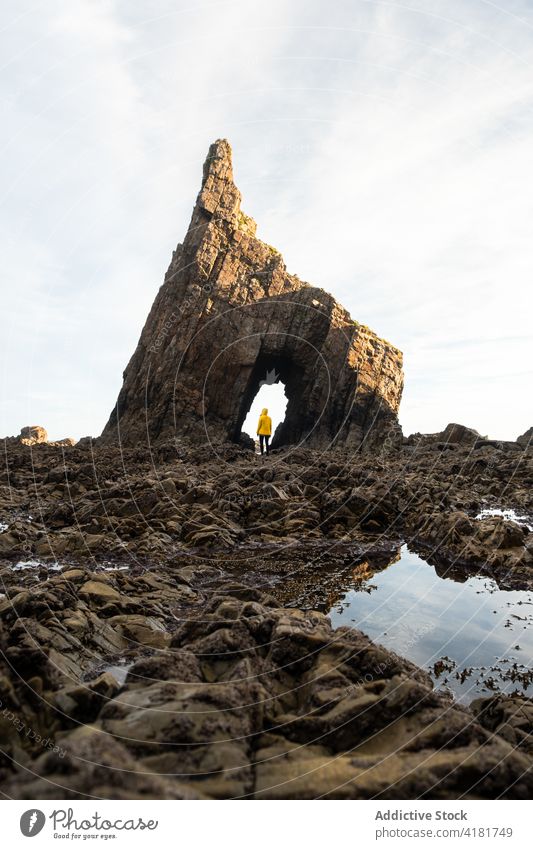 Person, die im Bogen einer natürlichen Felsformation am Ufer steht Reisender Felsen Golfloch erkunden Berge u. Gebirge Formation rau Hochland Herbst Geologie