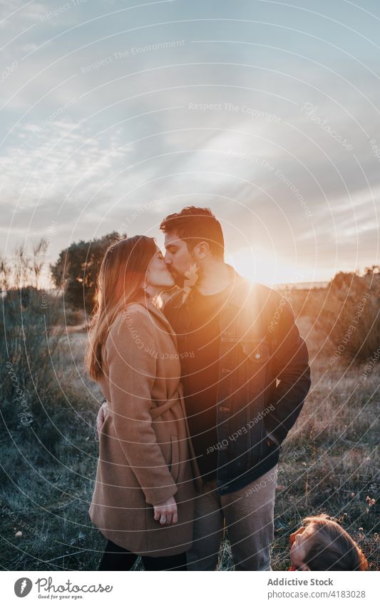 Paar küsst sich im Feld mit Kind bei Sonnenuntergang Kuss Familie Liebe Partnerschaft Angebot Natur Wochenende Augen geschlossen Glück Bonden Zuneigung Himmel