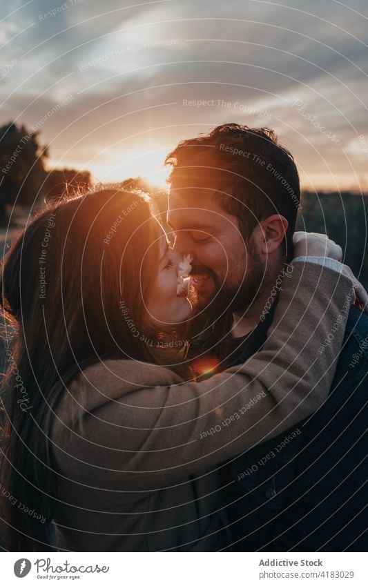 Paar küsst sich im Feld mit Kind bei Sonnenuntergang Kuss Familie Liebe Partnerschaft Angebot Natur Wochenende Augen geschlossen Glück Bonden Zuneigung Himmel