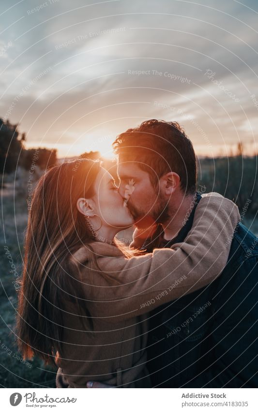 Paar küsst sich im Feld mit Kind bei Sonnenuntergang Kuss Familie Liebe Partnerschaft Angebot Natur Wochenende Augen geschlossen Glück Bonden Zuneigung Himmel