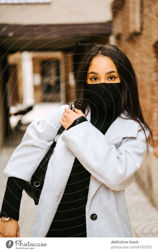 Moderne Frau in Maske mit Tasche auf der Straße Mantel selbstbewusst Mundschutz neue Normale urban Pandemie Stil Großstadt führen COVID19 Coronavirus Bund 19