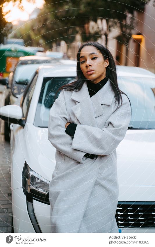 Selbstbewusste ethnische Frau an weißem Auto in der Stadt PKW selbstbewusst trendy Straße modern Stil Besitzer Fahrer anlehnen cool Zentrum Großstadt jung