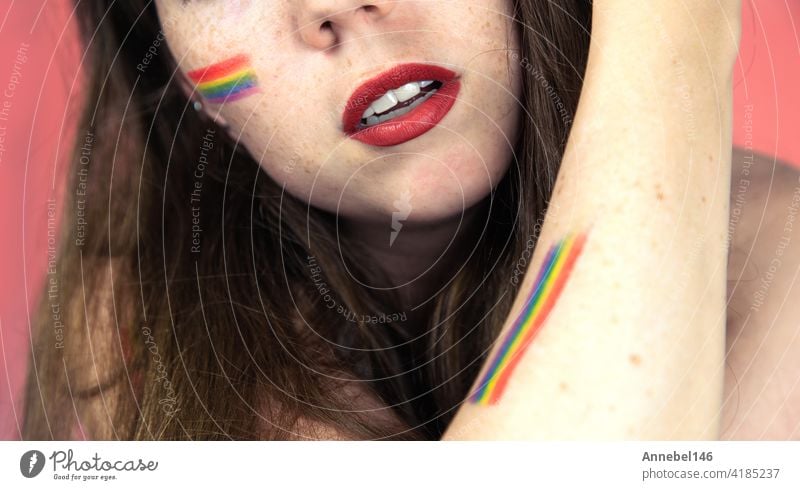 Porträt einer jungen Frau mit Regenbogen Flagge auf Wange und Körper, die LGBT-Gemeinschaft auf einem bunten rosa Hintergrund Mode Hand Pastell Liebe Person