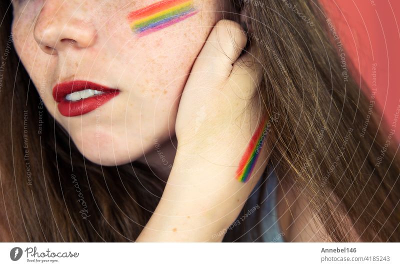 Porträt einer jungen Frau mit Regenbogen Flagge auf Wange und Körper, die LGBT-Gemeinschaft auf einem bunten rosa Hintergrund Mode Hand Pastell Liebe Person