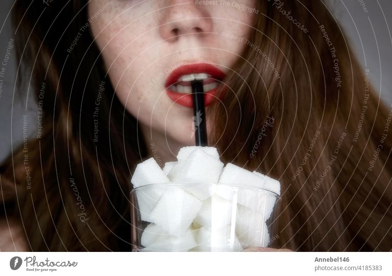 Porträt einer jungen Frau, die mit einem schwarz gefärbten Strohhalm aus einem mit Zuckerwürfeln gefüllten Glas trinkt Junk Food, ungesunde Ernährung, zu viel Zucker in Getränken, Ernährungskonzept