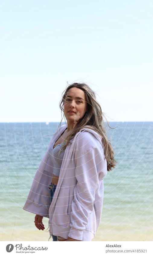 Schönes blondes Mädchen steht am Strand der Ostsee und schaut in die Kamera Lächeln freudig Landschaft durch Freude Außenaufnahme Gesicht Junge Frau hübsch