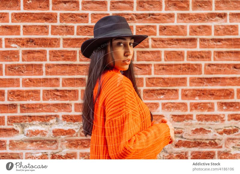 Stilvolle Frau mit Hut steht in der Nähe von Backsteinmauer Mode Strickwaren trendy Farbe hell orange jung ethnisch gestrickt Lifestyle Backsteinwand