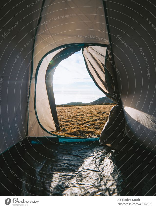 Durch die Zelttür des grasbewachsenen Geländes in der Nähe von Hügeln im Sonnenlicht Lager Wiese Natur Campingplatz Tourismus Wanderung Ausflug friedlich wolkig