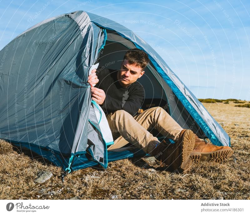 Seriöser junger Mann, der sich während eines Wanderausflugs im Zeltlager entspannt ruhen Lager Trekking Reisender trendy ernst Natur Fernweh Wanderung männlich