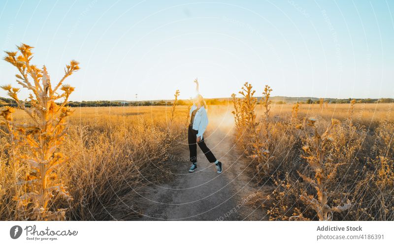 Stilvolle junge Frau tanzt auf dem Lande im Sonnenlicht Tanzen Feld Landschaft Natur sich[Akk] bewegen selbstbewusst aktiv Feiertag Pflanze trendy trocknen Gras