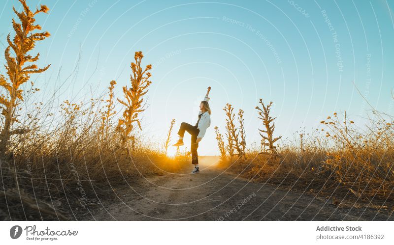 Stilvolle junge Frau tanzt auf dem Lande im Sonnenlicht Tanzen Feld Landschaft Natur sich[Akk] bewegen selbstbewusst aktiv Feiertag Pflanze trendy trocknen Gras