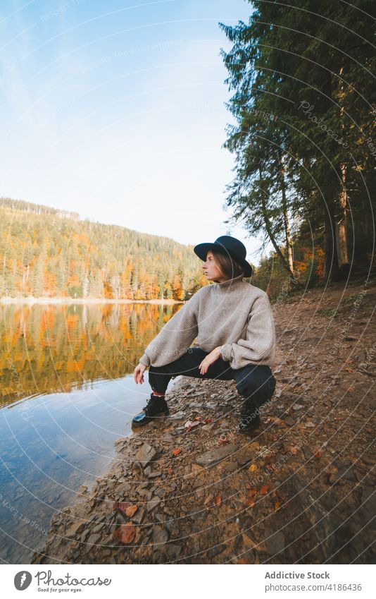 Stilvoller Reisender hockt am Ufer gegen den reinen See Tourist cool Natur Baum Reflexion & Spiegelung Urlaub Frau Hut lässig Bekleidung Ausflug Kleidungsstück