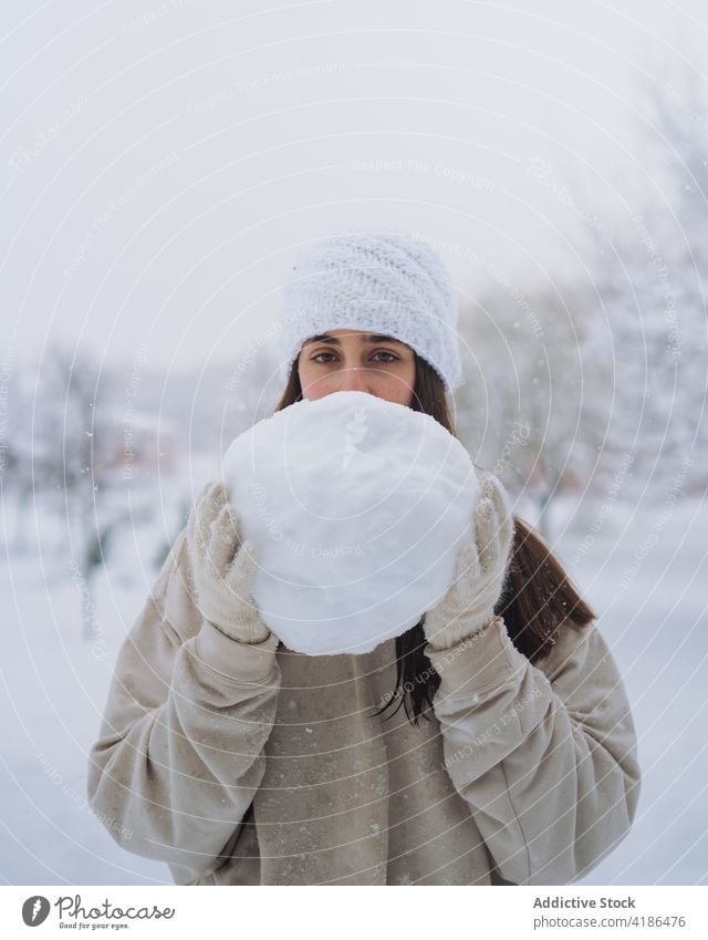 Lächelnde ethnische Frau mit Schneeball in winterlicher Stadt Winter genießen Zeitvertreib Wochenende Park Großstadt Himmel zeigen freie Zeit vegetieren kalt