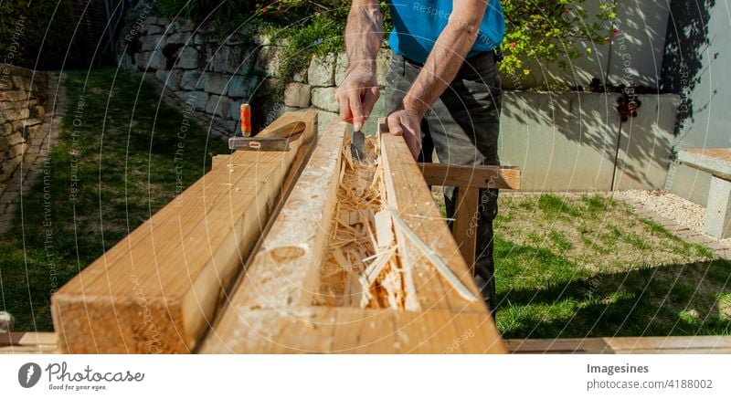 Holzarbeiten. Hohlbalken mit Meißeln aushöhlen. Schreiner verarbeitet einen Holzbalken Fräsen Werkstatt Außen Garten Farbbild horizontal Arbeitsgerät Zimmerei