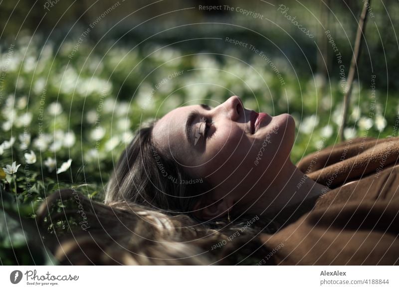 Ein schönes blondes Mädchen liegt auf einer Waldlichtung in einer grünen Blumenwiese mit geschlossenen Augen und lächelt Lächeln freudig Landschaft Freude