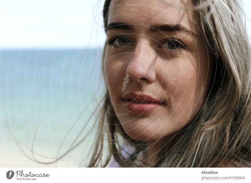 Schönes blondes Mädchen steht am Strand der Ostsee und schaut in die Kamera Lächeln freudig Landschaft Freude Außenaufnahme Gesicht Junge Frau hübsch beschwingt