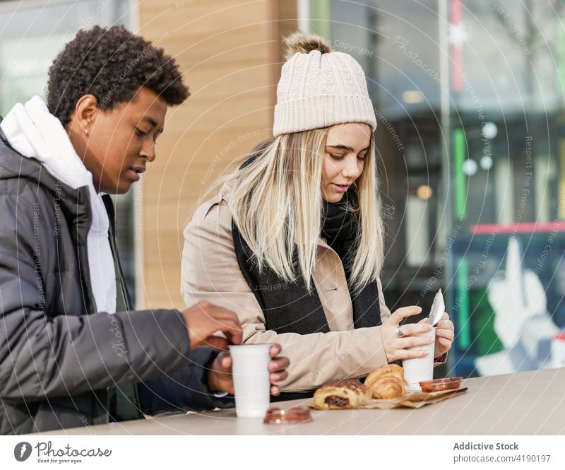 Multirassische Partner mit Kaffee zum Mitnehmen und Gebäck im Cafe Kaffeepause Zeit verbringen lecker Café Straße Porträt Frau Mann gebacken geschmackvoll Glas